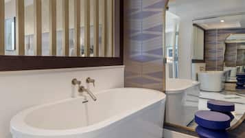 Un baño moderno con una bañera independiente, un espejo grande y un revestimiento de pared con estampado geométrico.