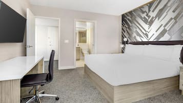 A hotel room with a bed, a desk, and a chair. There is a bathroom visible through an open door.