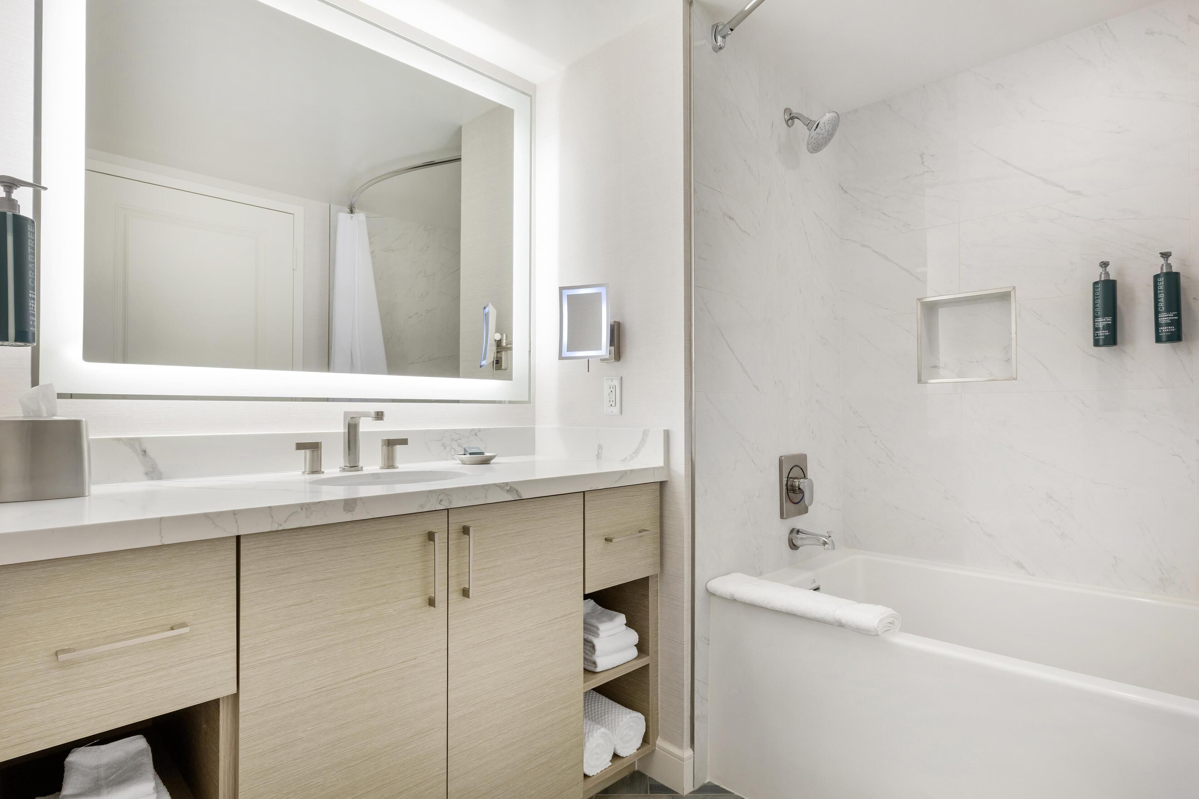 A modern bathroom with a large mirror, two sinks, a shower, and a bathtub.