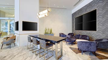 Un interior moderno con suelo de mármol, una mesa de comedor central con sillas, un conjunto de sofás y un televisor grande montado en la pared.