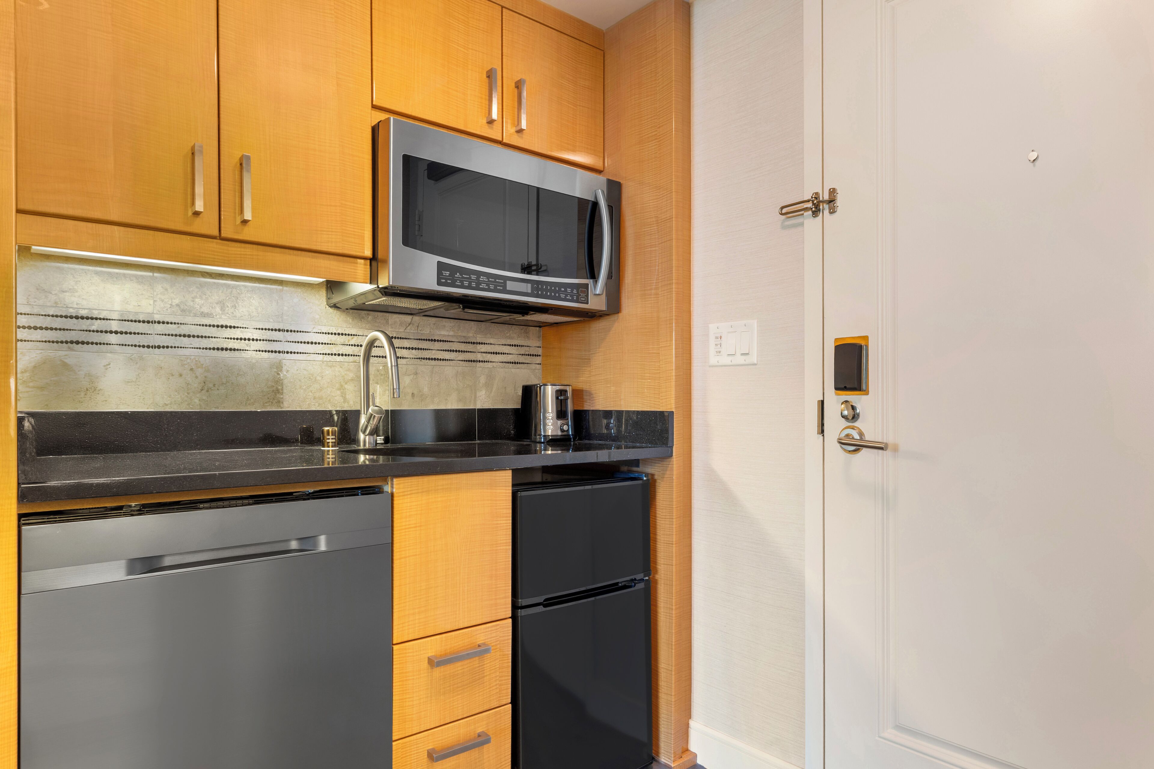 A kitchen with wooden cabinets, a stainless steel refrigerator, a microwave, and a black countertop.