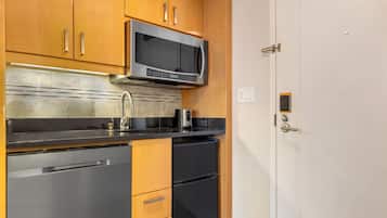 A kitchen with wooden cabinets, a stainless steel refrigerator, a microwave, and a black countertop.