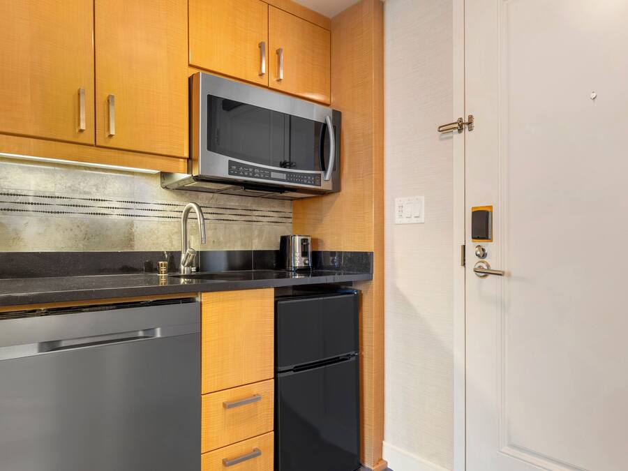 A kitchen with wooden cabinets, a stainless steel refrigerator, a microwave, and a black countertop.