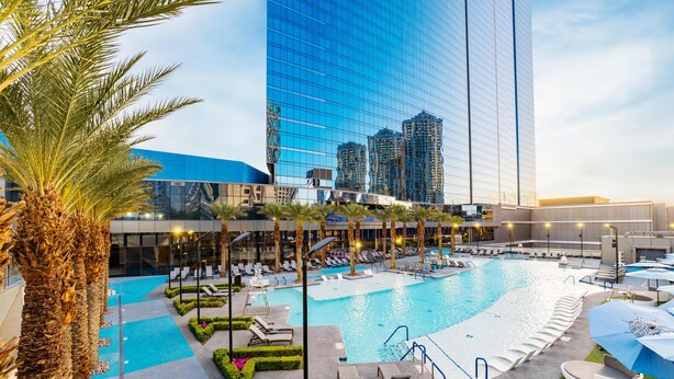 A hotel pool area with lounge chairs, a swimming pool, and a tall building in the background.