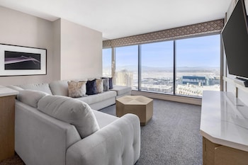 A modern hotel room with a large bed, a desk, a chair, and a TV. The room has large windows with a city view. at Hilton Grand Vacations Club Elara Center Strip Las Vegas