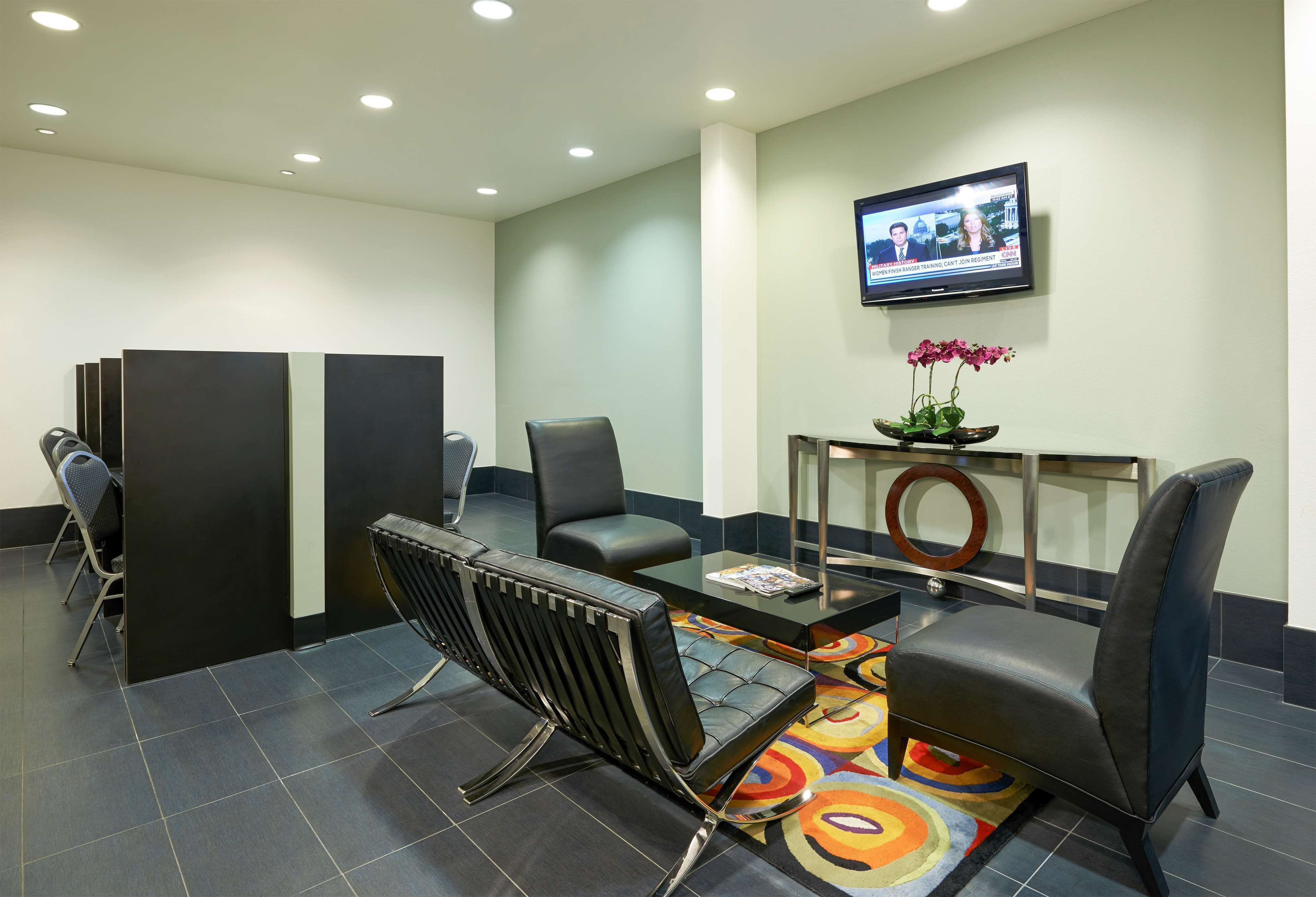 A modern waiting area with a TV, comfortable seating, and a small table with a vase of flowers.