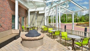 An outdoor patio with a glass enclosure, green chairs, and a stone fire pit. - SpringHill Suites by Marriott Fairfax Fair Oaks (Fairfax)