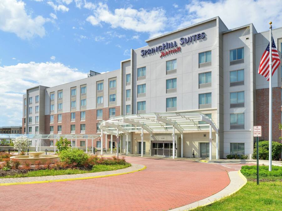 Un hotel SpringHill Suites Marriott con ingresso coperto, una fontana e una bandiera americana.