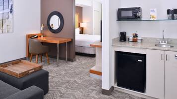 A hotel room with a kitchenette, a bed, a desk, and a seating area.