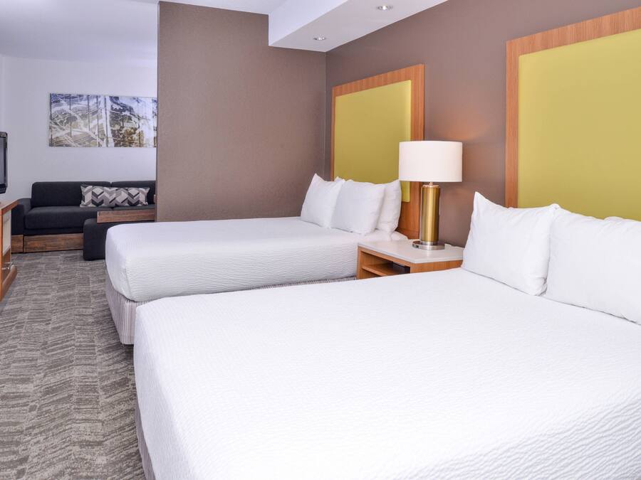 A hotel room with two beds, a TV, a sofa, and a painting on the wall.