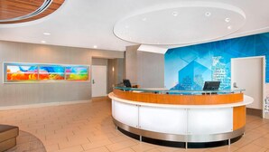 A modern reception area with a curved reception desk, a large abstract painting on the wall, and a digital screen. - SpringHill Suites by Marriott Fairfax Fair Oaks (Fairfax)