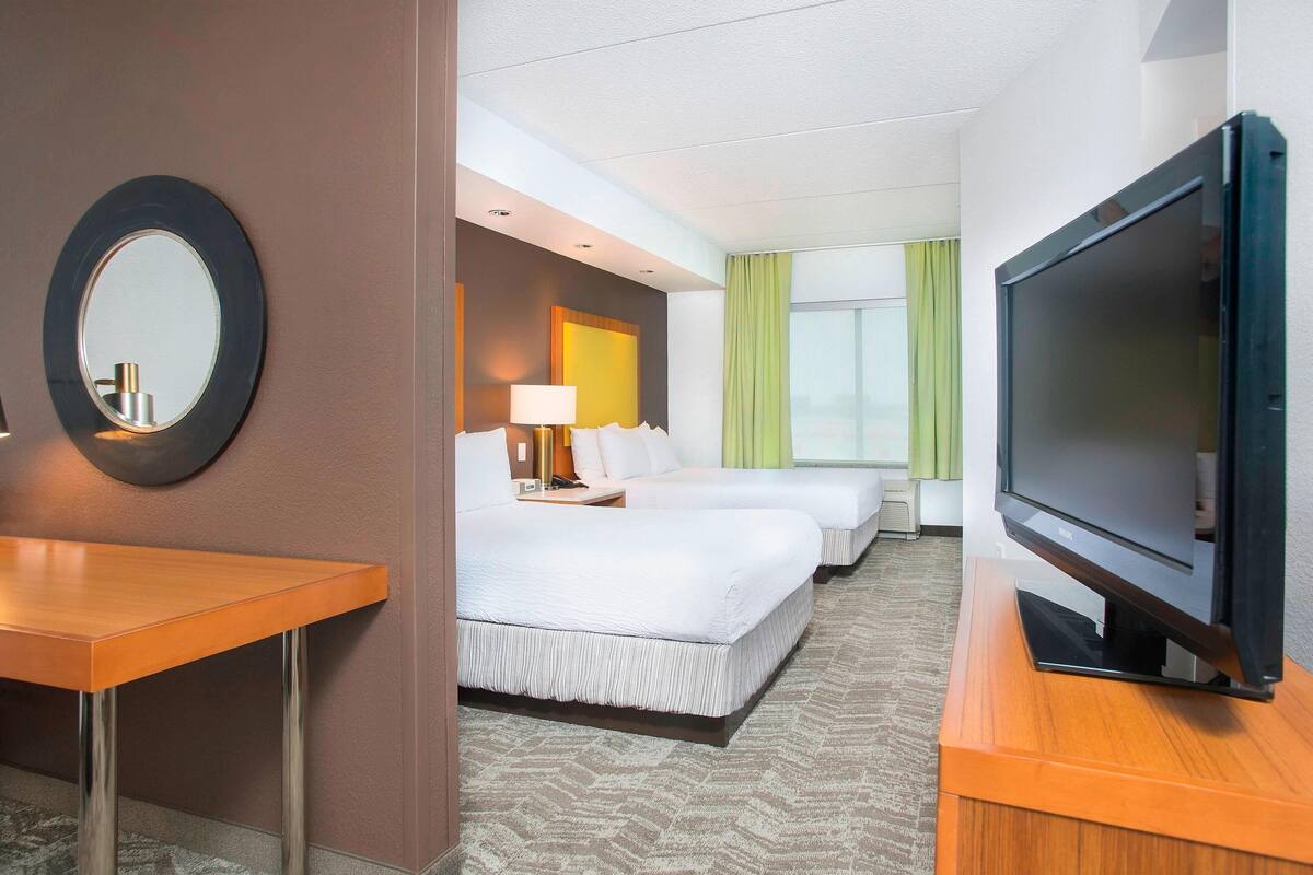 Habitación de hotel con cama, televisor, escritorio y espejo.