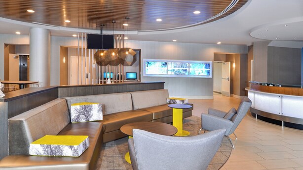 A modern lobby with a seating area, a reception desk, and a large screen displaying information. - SpringHill Suites by Marriott Fairfax Fair Oaks (Fairfax)