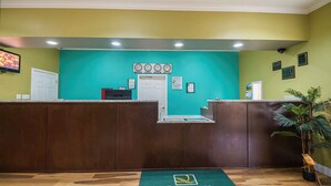A reception area with a teal wall, wooden reception desk, and a green carpet with the Quality Inn logo. - Quality Inn DeRidder (DeRidder)