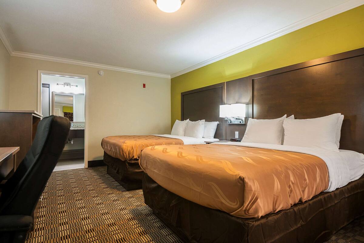 A hotel room with two beds, a desk, and a chair.