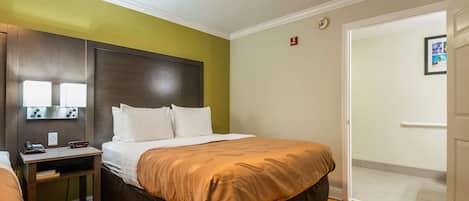 Habitación de hotel con cama, mesita de noche y velador. Se ve una puerta que da a otra habitación.