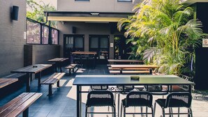 An outdoor patio area with wooden benches and tables, surrounded by a building with a flat roof and windows. - Best Western Blackbutt Inn (New Lambton)