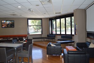 Amplio espacio interior con diversas opciones de asientos, incluyendo mesas, sillas y sofás. Amplias ventanas ofrecen luz natural y vistas al exterior.