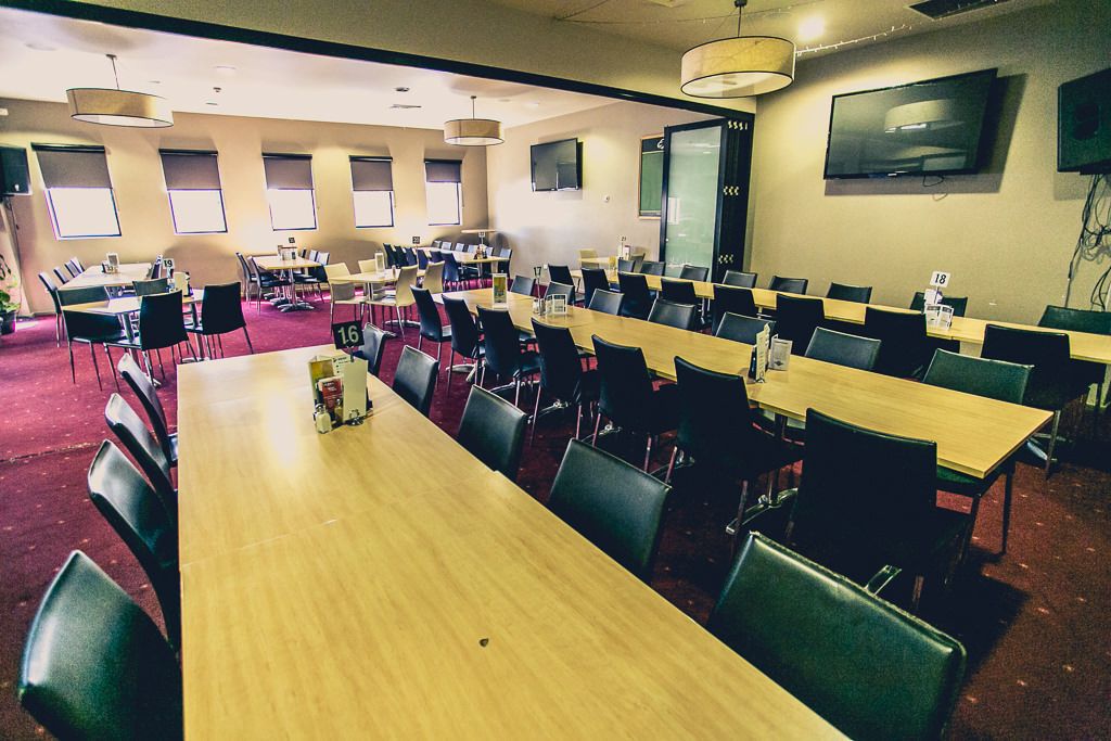 A conference room with multiple tables and chairs, numbered seating, and a large screen on the wall.
