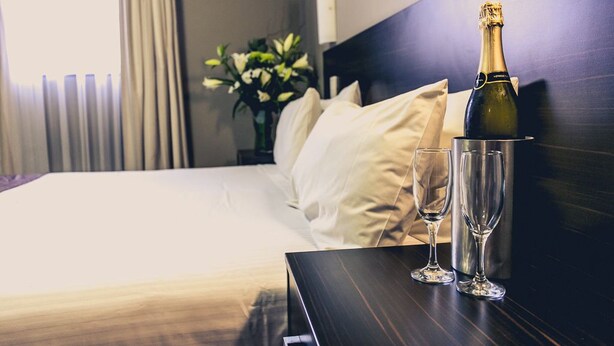 A hotel room with a bed, a bedside table with a bottle of champagne and two glasses, a vase with flowers, and a view of the outside. - Best Western Blackbutt Inn (New Lambton)