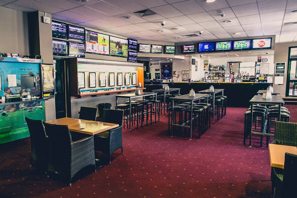 Un restaurante con varias mesas y sillas, una zona de bar y varios monitores mostrando contenido.