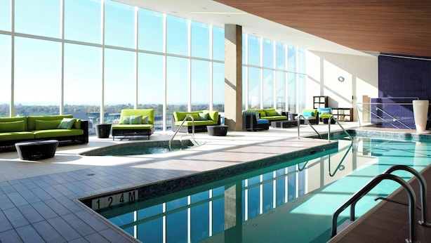 A modern indoor pool area with large windows, green sofas, and a clear view of the city. - Montreal Airport Marriott In-Terminal Hotel (Dorval)