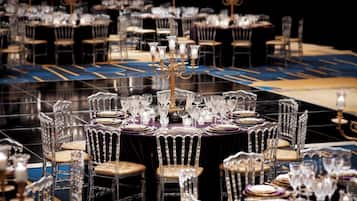 Un salón de banquetes con mesas redondas dispuestas para un evento formal, con sillas transparentes y elegantes centros de mesa.