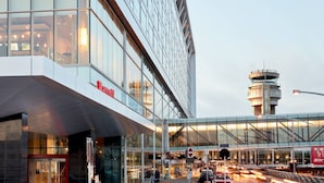 A modern hotel with a glass facade, a prominent entrance, and a view of the airport control tower in the background. - Montreal Airport Marriott In-Terminal Hotel (Dorval)