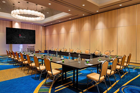 Un salón de conferencias con una larga mesa, sillas, una pantalla grande y piso alfombrado.