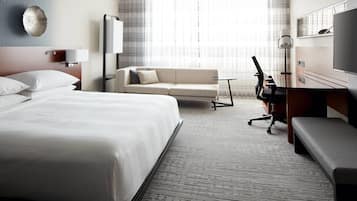 Een hotelkamer met een groot bed, een slaapbank, een bureau met een stoel en een televisie.