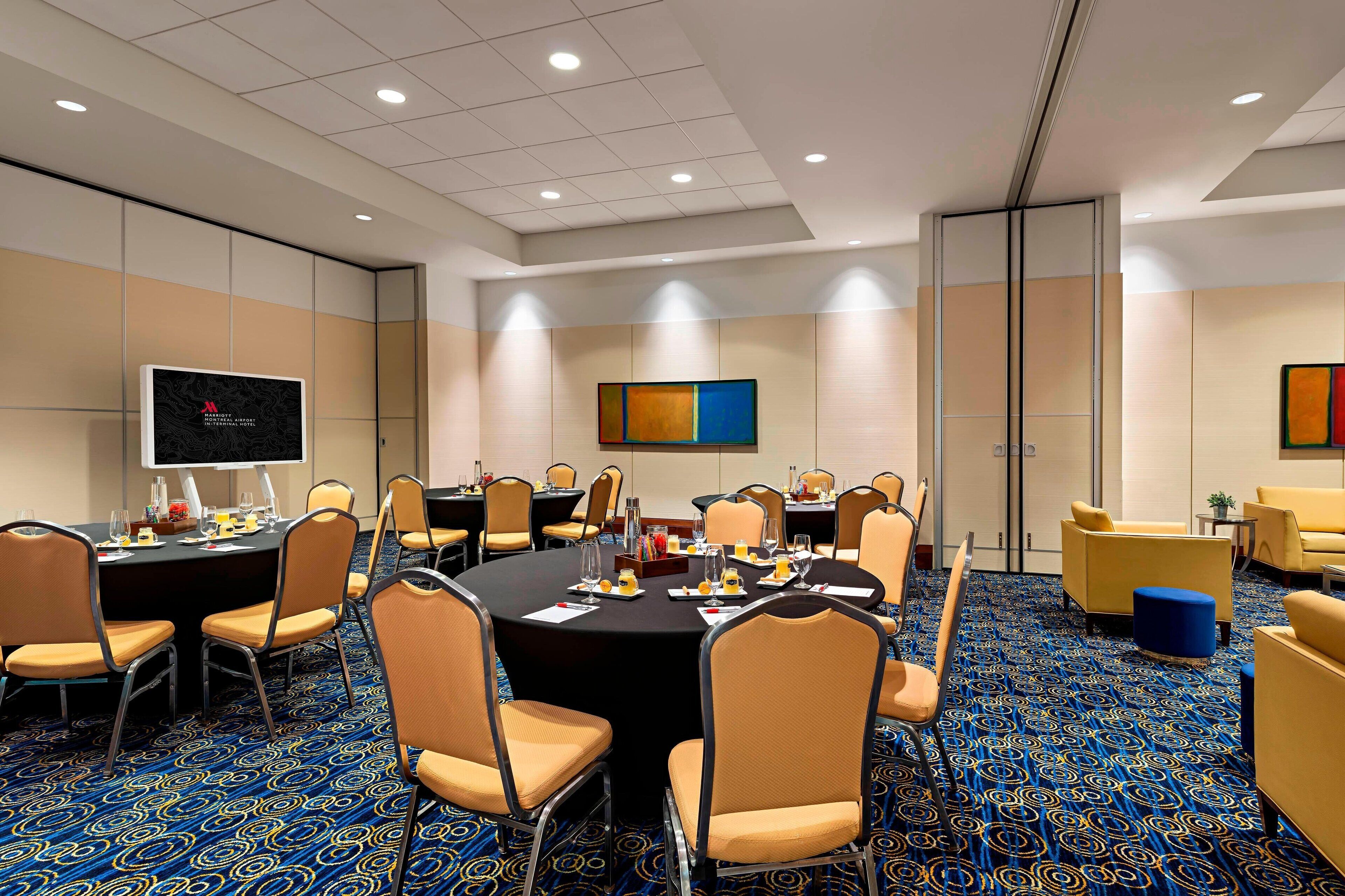 A conference room with a large table, chairs, a TV screen, and a carpeted floor.