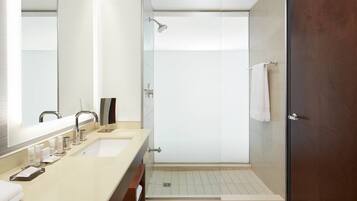 A modern bathroom with a double sink, a large mirror, a shower with a glass door, and a wooden door.