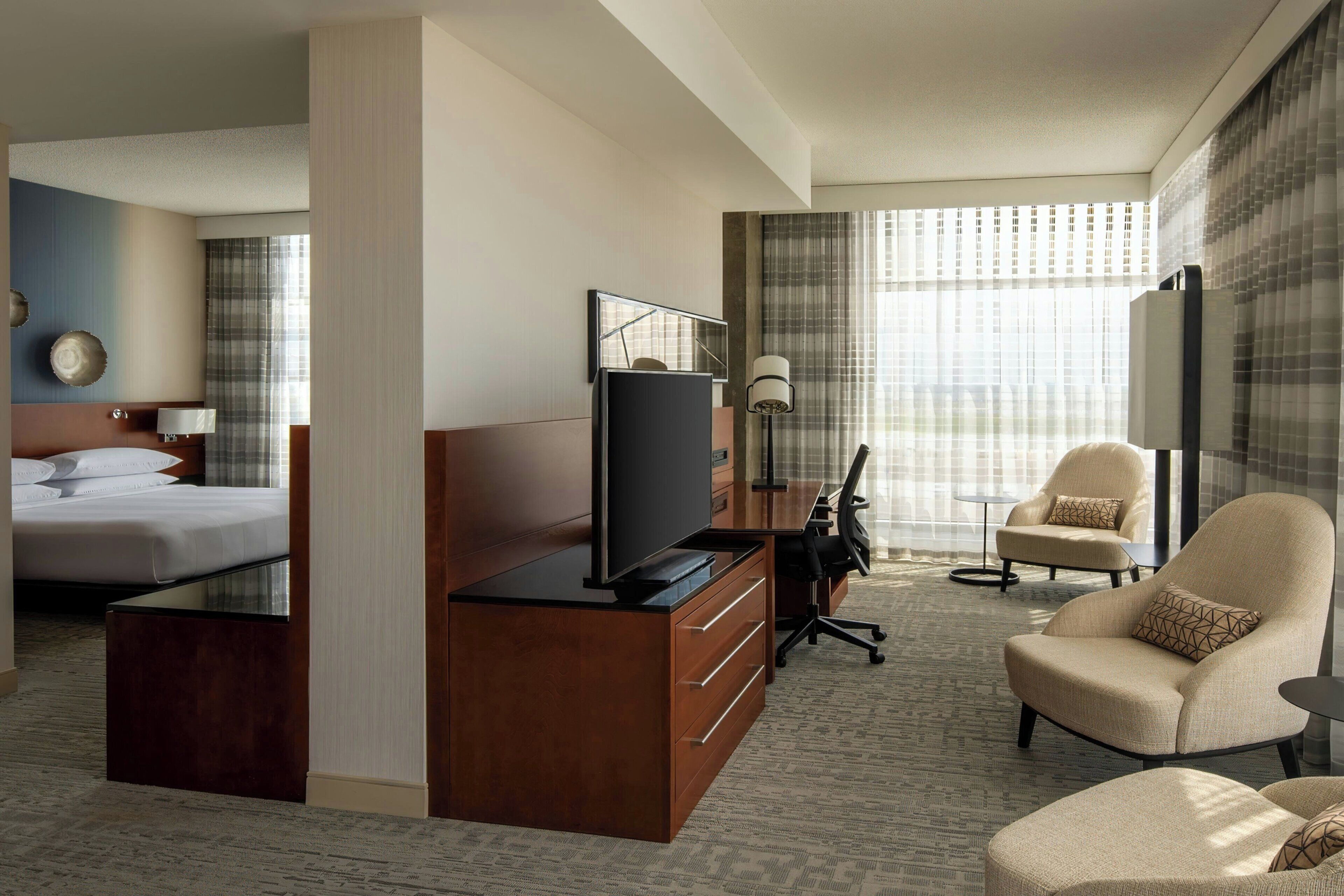 Quarto de hotel com cama, escrivaninha com televisão, poltrona e sofá.
