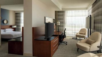 Quarto de hotel com cama, escrivaninha com televisão, poltrona e sofá.
