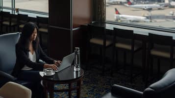 A woman working on a laptop in a hotel room with a view of the airport.