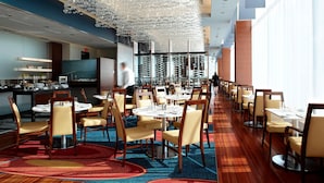 A modern dining area with round tables, chairs, and a unique ceiling design. - Montreal Airport Marriott In-Terminal Hotel (Dorval)