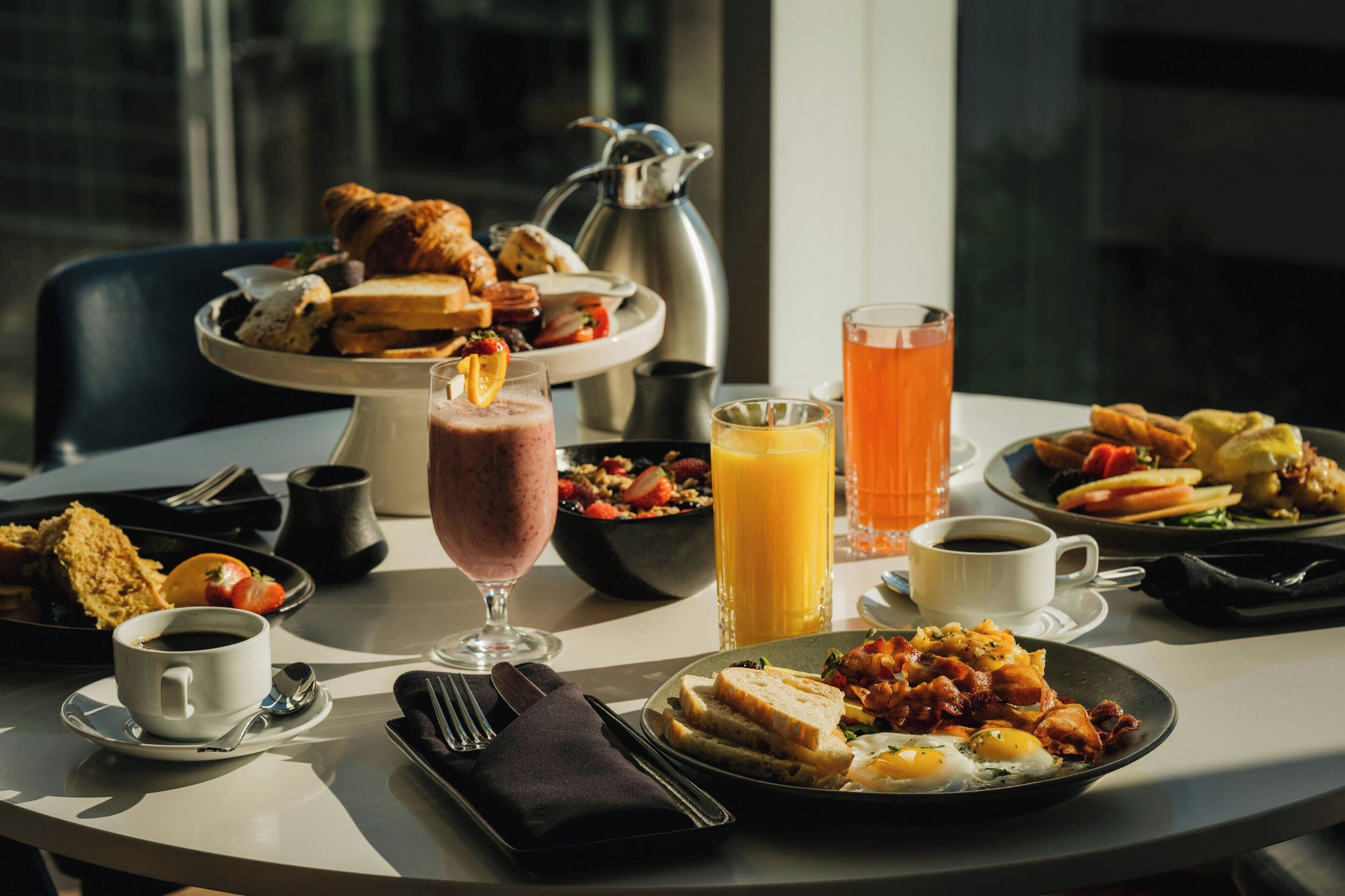 A breakfast setting with various dishes, drinks, and a coffee pot on a table.