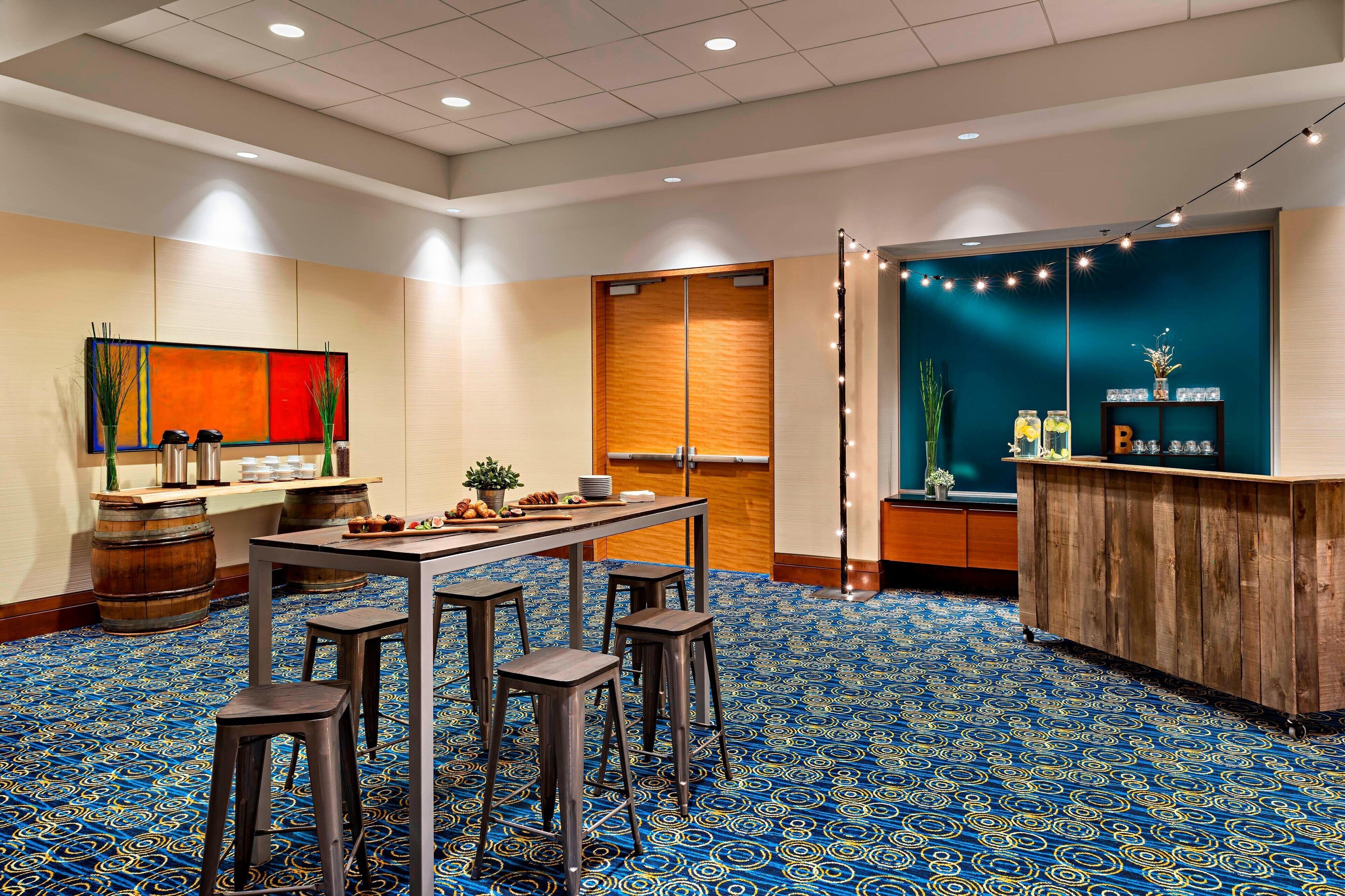 Une chambre d’hôtel dotée d’une grande fenêtre, d’un bureau en bois, d’un coin bar et d’une moquette à motifs.