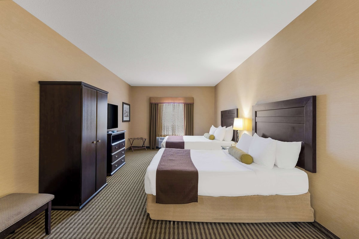 A hotel room with two beds, a wardrobe, a bench, and a desk with a lamp.