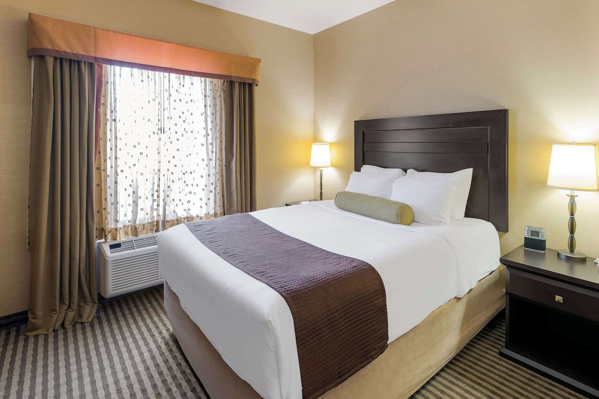 A hotel room with a large bed, two bedside lamps, a nightstand, and a window with curtains.