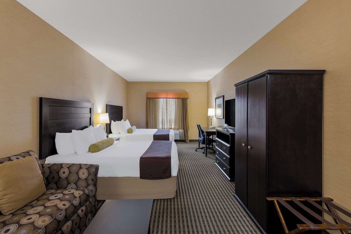 A hotel room with two beds, a sofa, a desk, and a wardrobe.