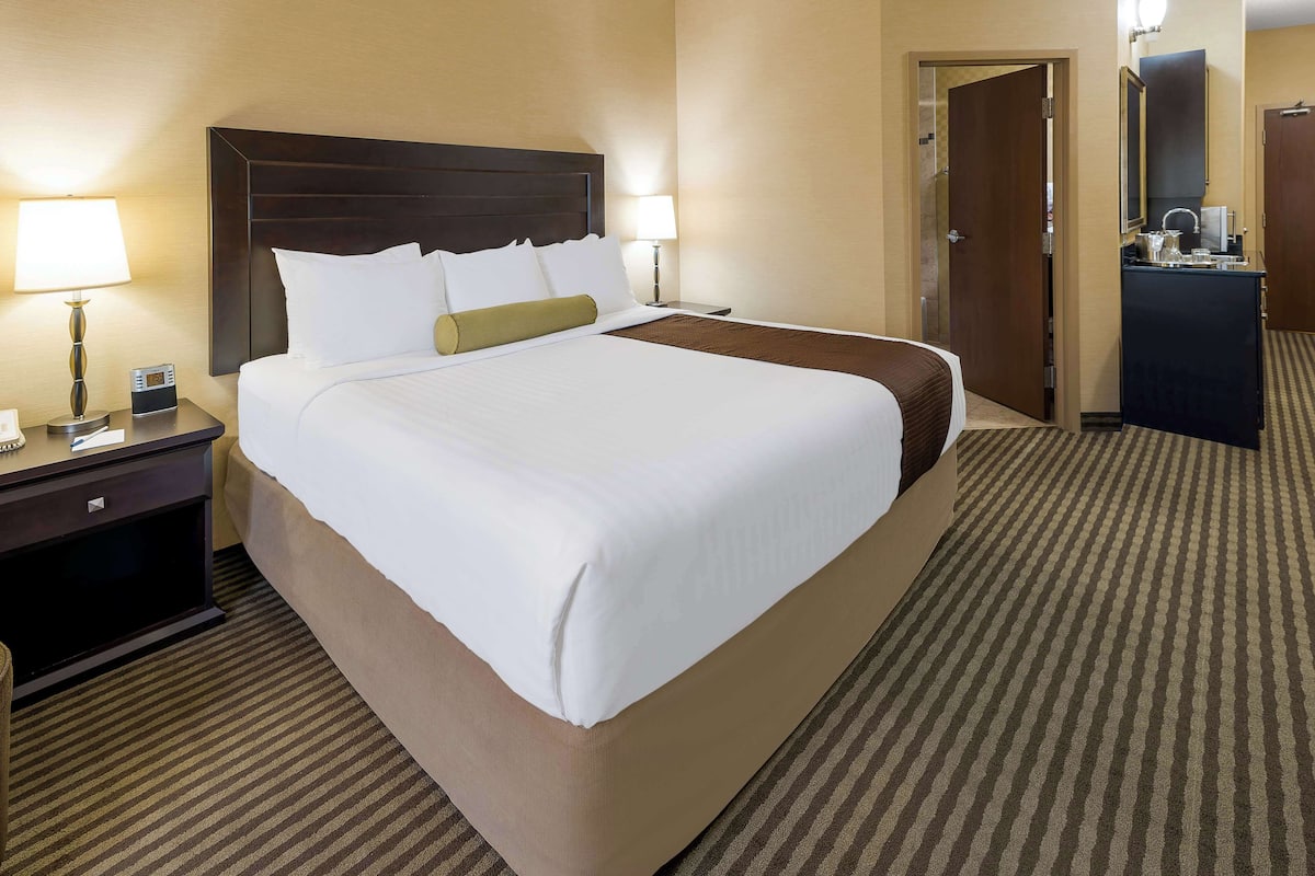 A hotel room with a large bed, two bedside tables with lamps, a dresser, and a door leading to another room.