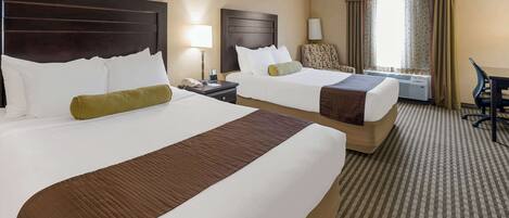 A hotel room with two beds, a desk, a chair, a lamp, and an air conditioning unit.