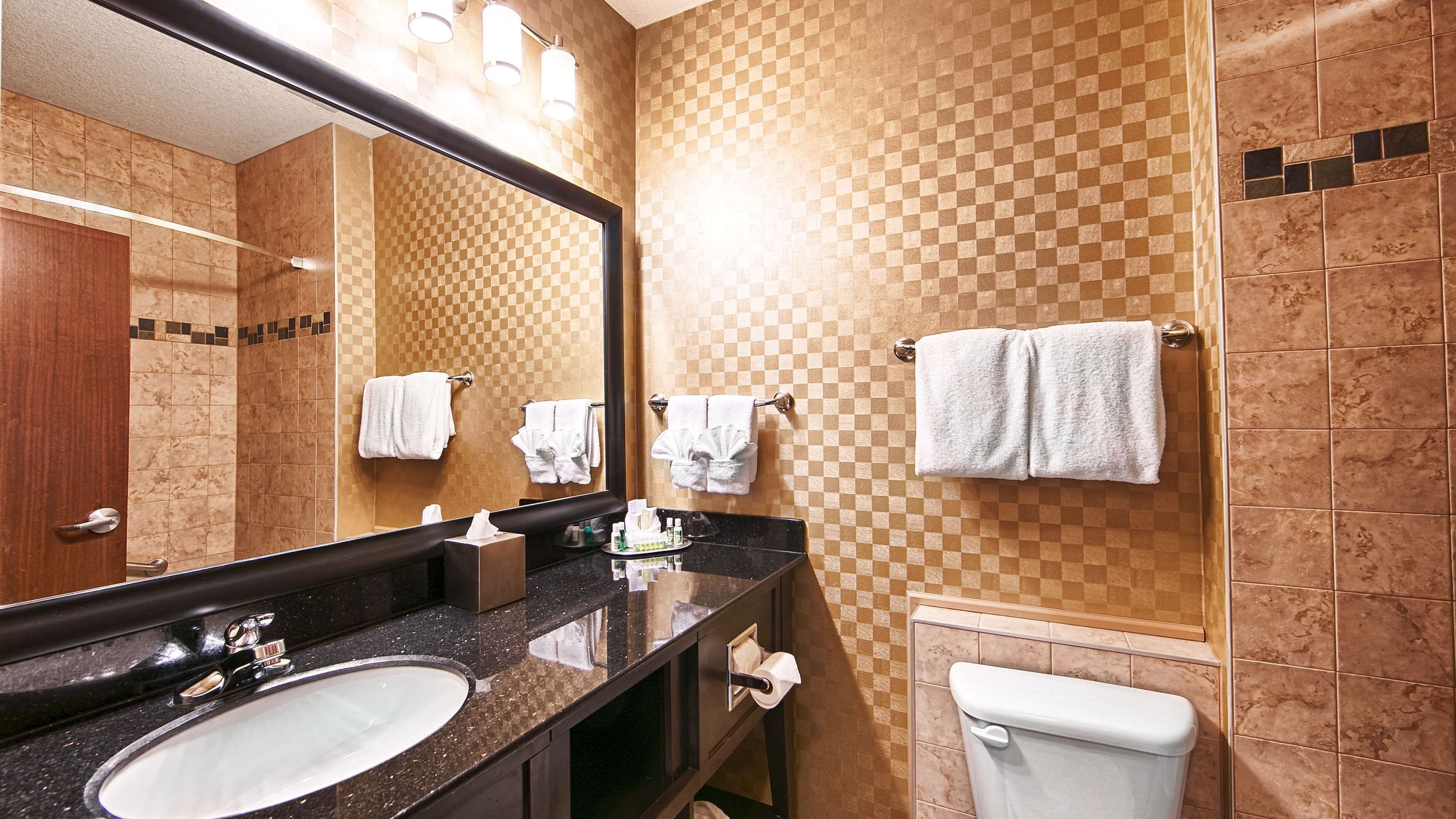 A hotel bathroom with a large mirror, a sink, a toilet, and multiple towels hanging on the wall.