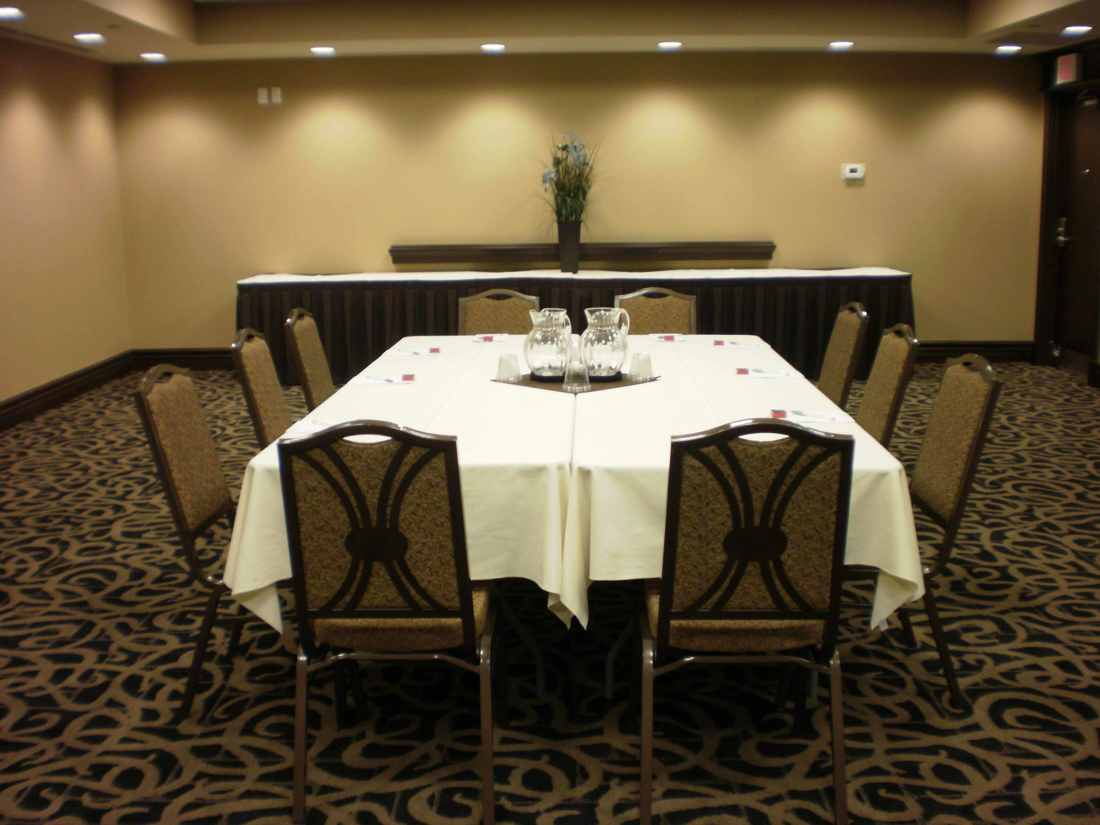 Une salle de conférence avec une table blanche, des chaises et un vase de fleurs.