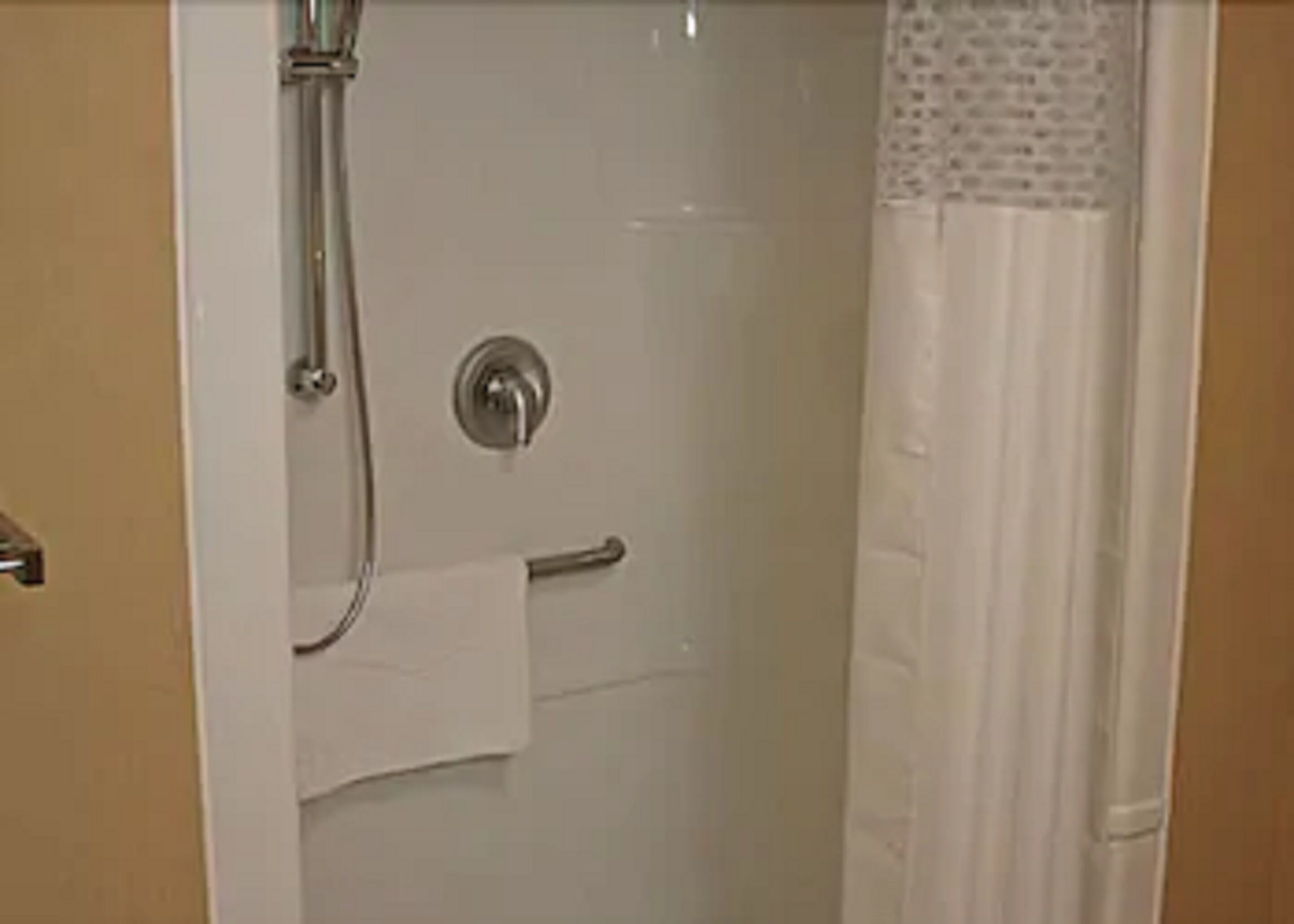 A bathroom with a shower, a towel rack, and a toilet paper holder.