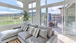 Una sala de estar moderna con un sofá seccional grande, una planta en maceta y vistas a un patio con mobiliario exterior.