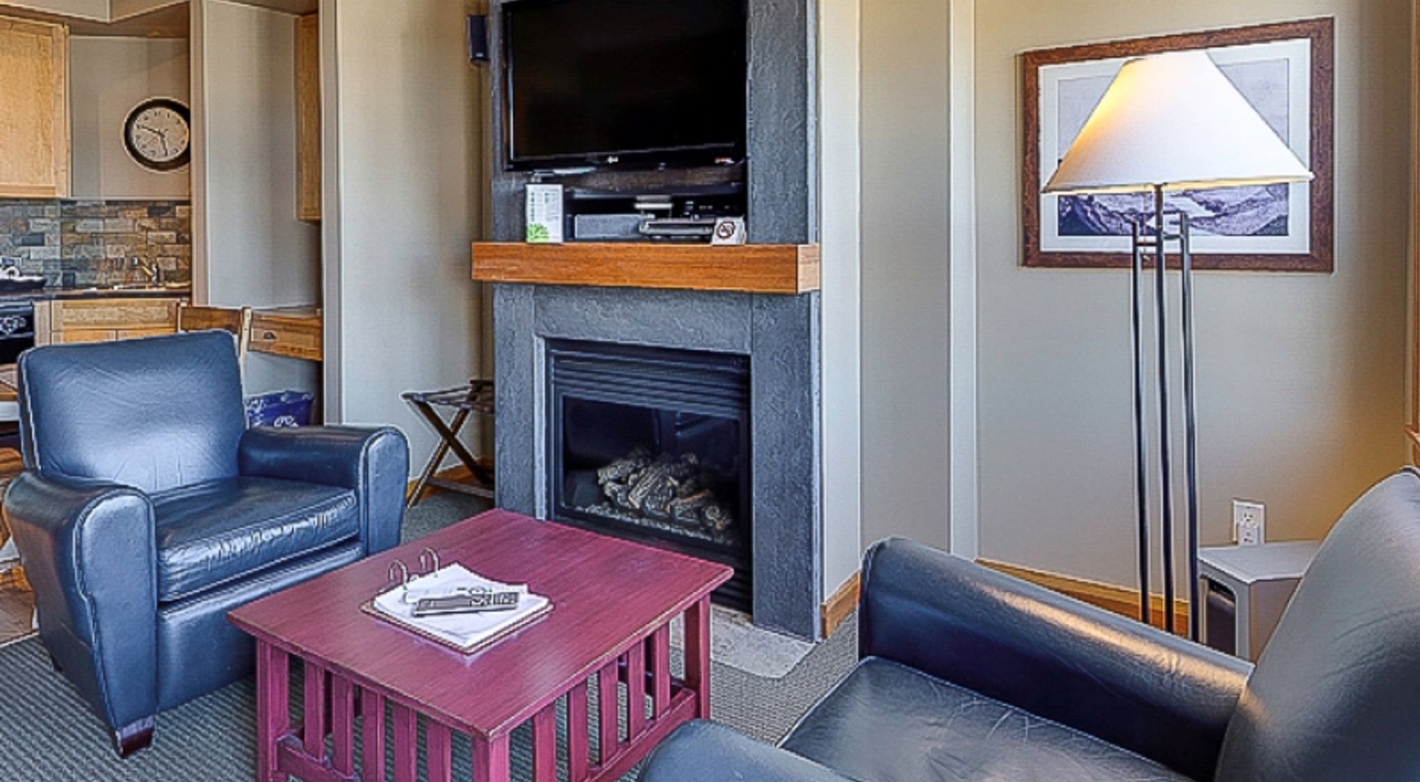 A living room with a fireplace, a flat-screen TV mounted above it, leather sofas, and a coffee table.