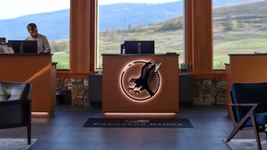 Un área de recepción con un gran techo de madera, una mesa de recepción con un logotipo y vistas del paisaje a través de amplios ventanales.