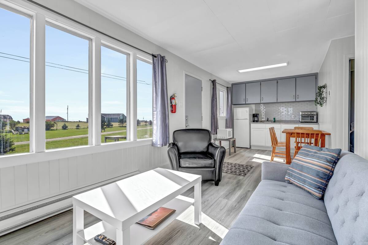 Ein modernes Wohnzimmer mit grauem Sofa, einem weißen Couchtisch und Blick ins Freie.